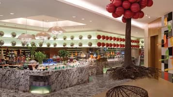 A hotel lobby with a marble reception desk, a large red balloon tree, and a modern chandelier.