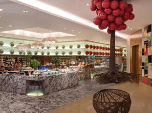 Un hall d’hôtel avec un comptoir d’accueil en marbre, un grand arbre décoré de ballons rouges et un lustre moderne.