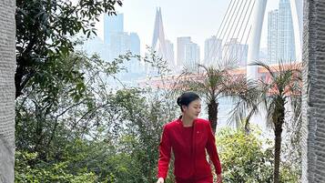 A person in a red dress walking on a stone pathway with a cityscape and a bridge in the background.