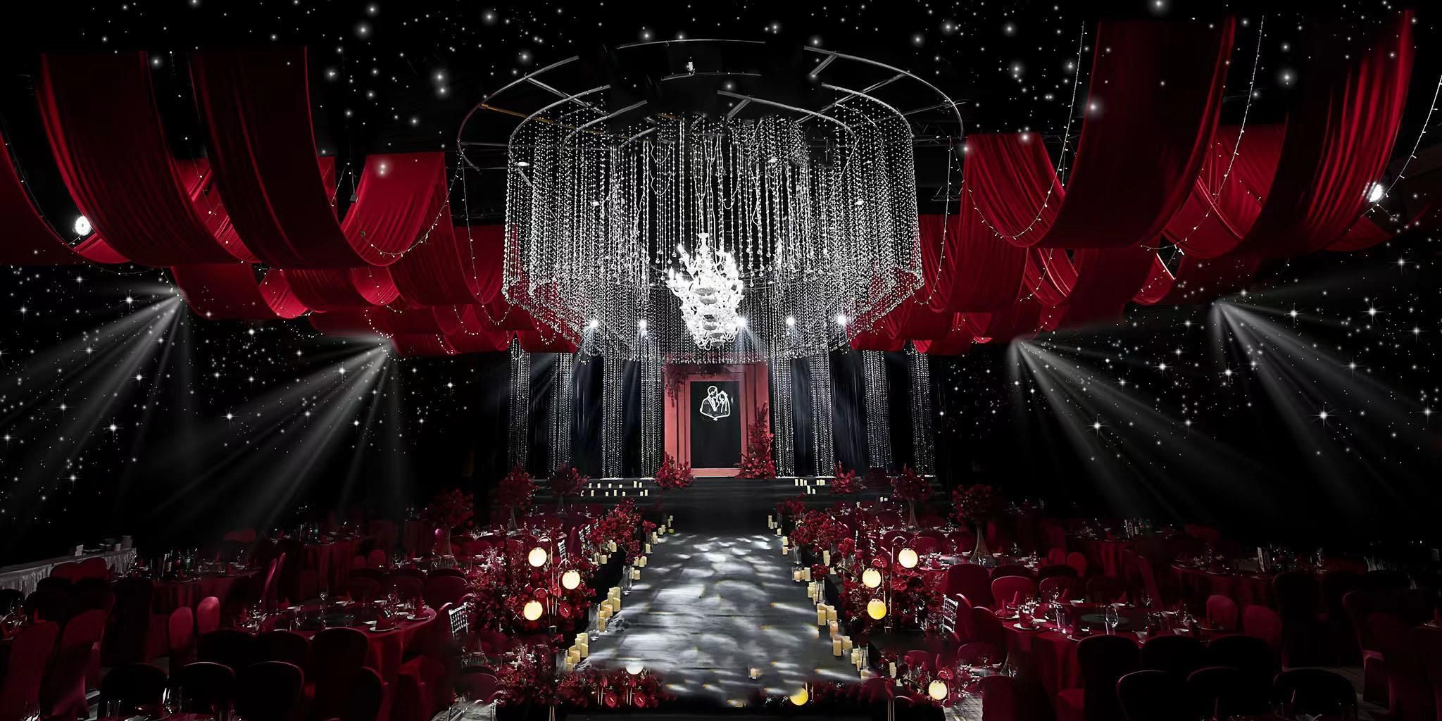 An indoor venue with a stage, red curtains, and a chandelier.