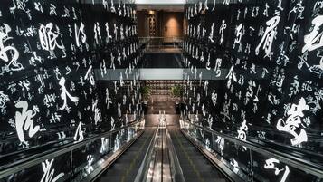 Un pasillo interior con escaleras mecánicas, flanqueado por paredes cubiertas de caligrafía blanca.