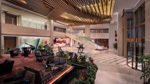 A spacious lobby with a grand piano, multiple seating areas, a staircase, and a large glass wall.