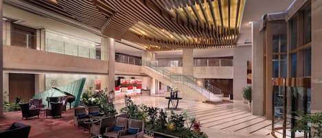 A spacious lobby with a grand piano, multiple seating areas, a staircase, and a large glass wall.