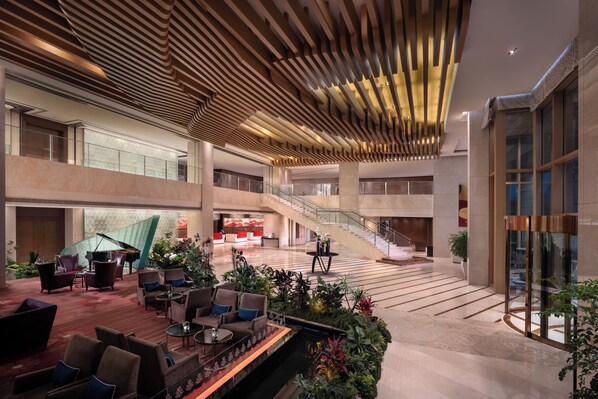 Un hall d’entrée spacieux, agrémenté d’un grand piano, de plusieurs espaces de détente, d’un escalier et d’un grand mur de verre.