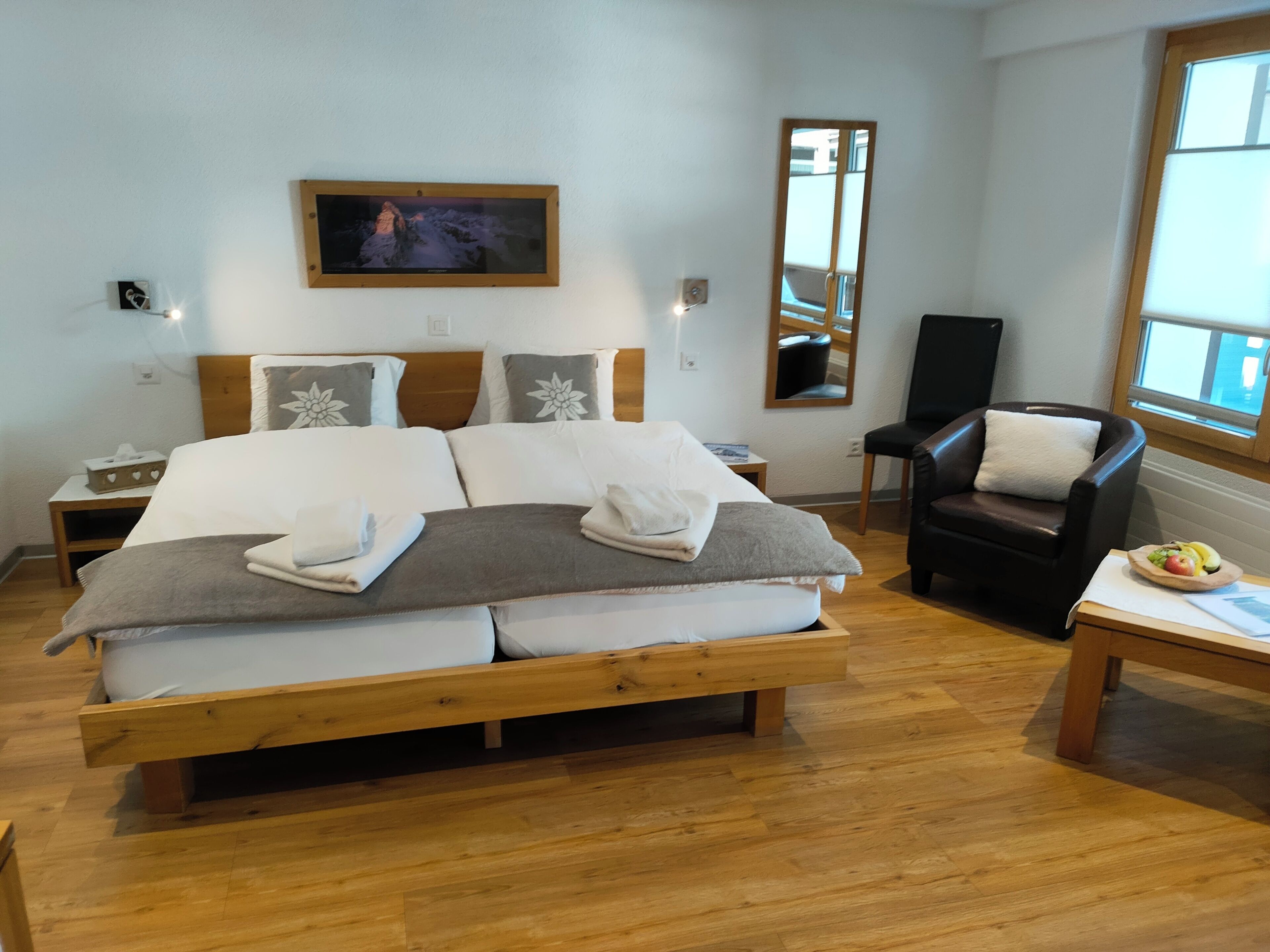 A bedroom with a wooden bed, a nightstand, a chair, and a small table with fruit.