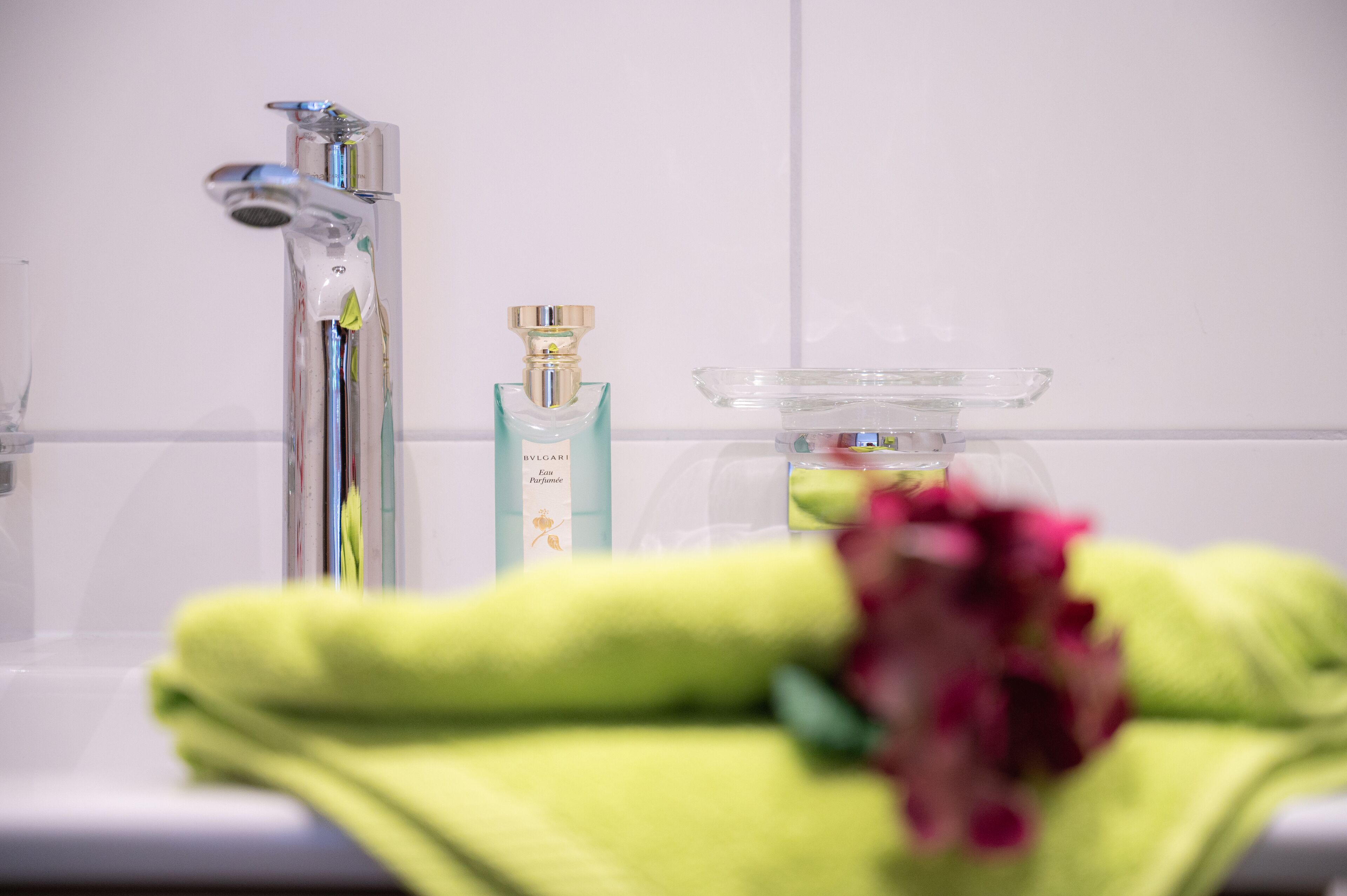 Un bagno con un moderno rubinetto, una bottiglia di profumo e un portasapone in vetro.