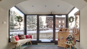 A cozy room with a bench, a wooden cabinet, and a view of a snowy landscape through large glass doors. - Jolimont Apartments (Zermatt)