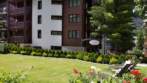 A well-maintained lawn with a row of sun loungers and a variety of flowers in the foreground. - Jolimont Apartments (Zermatt)