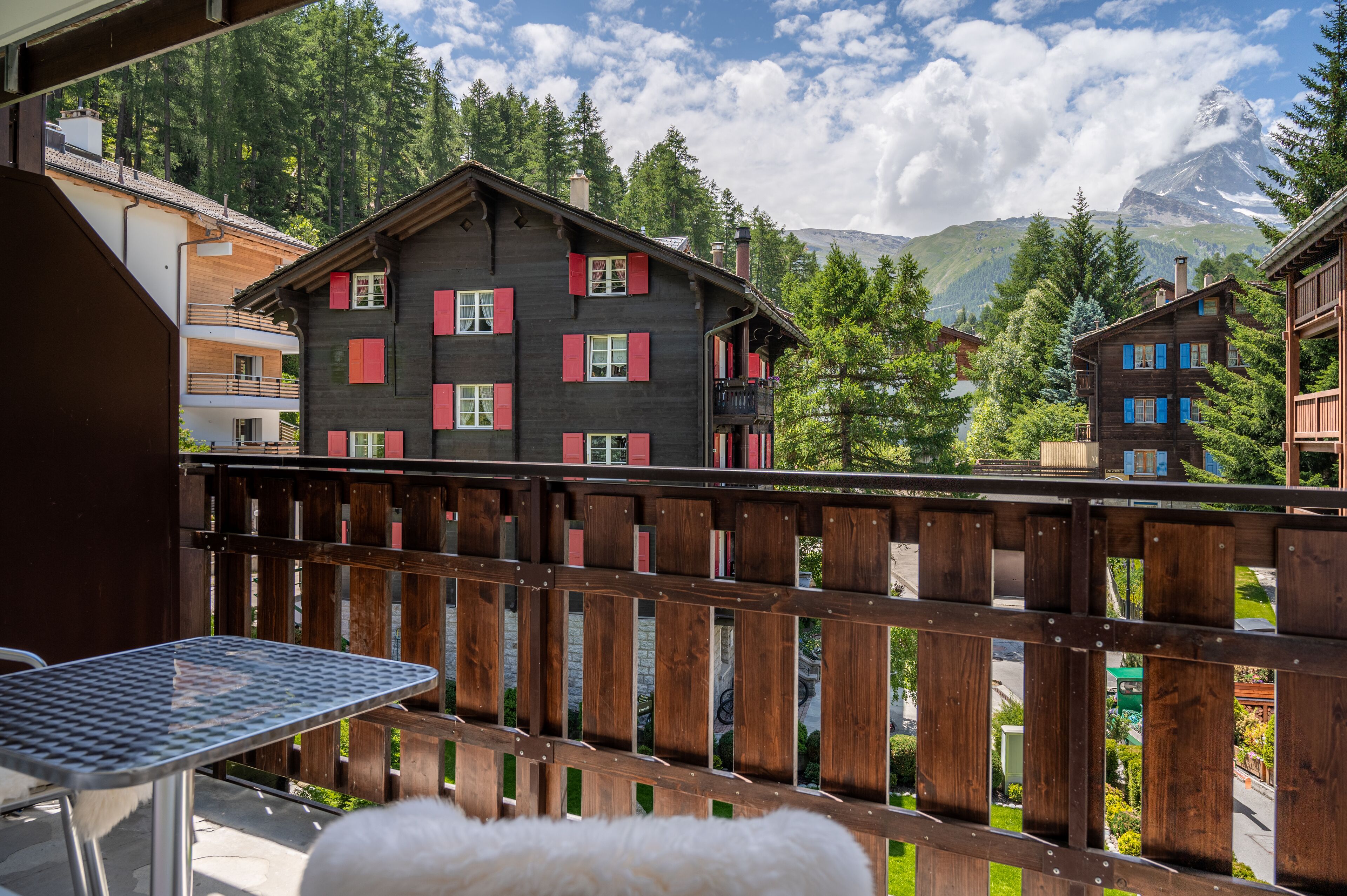 A wooden chalet with red shutters, a balcony, and a view of mountains.