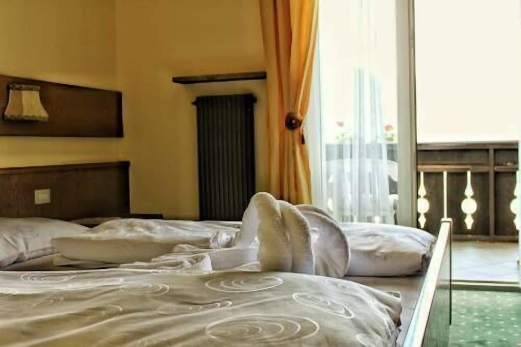 Une chambre d’hôtel avec un lit, une fenêtre avec des rideaux, un radiateur et un luminaire fixé au mur.