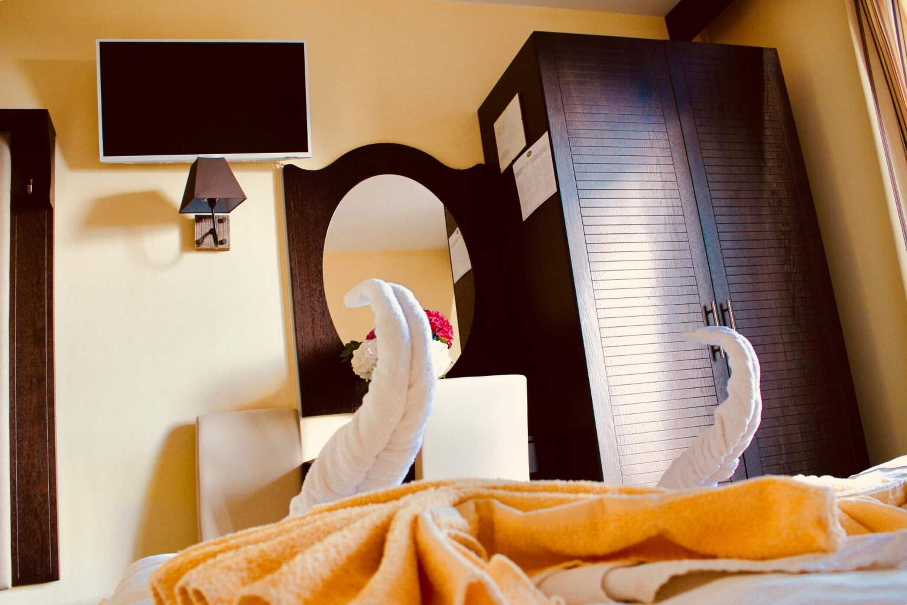 A hotel room with a bed, a television mounted on the wall, a mirror, and a wardrobe.