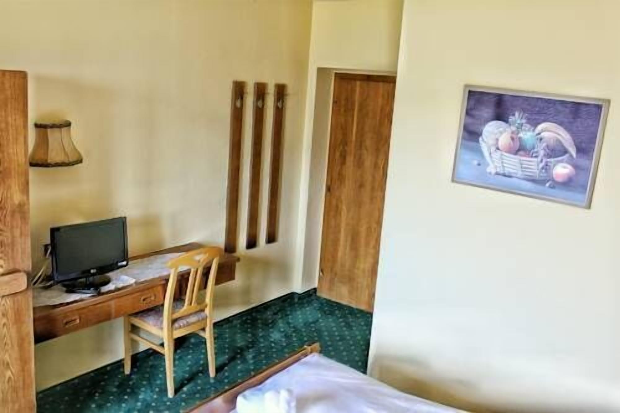 A small room with a bed, a desk with a chair, a television, and a framed picture on the wall.