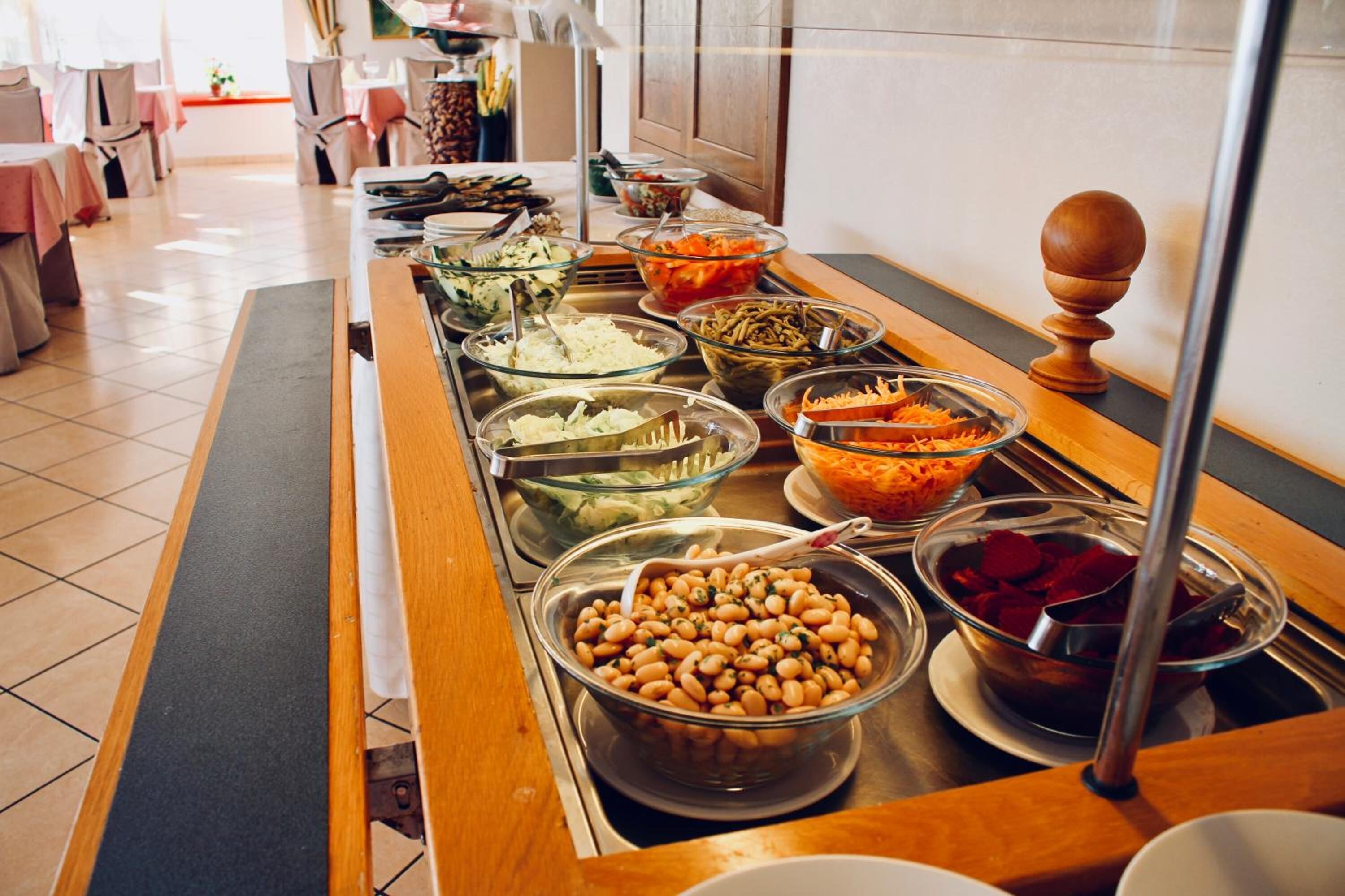 Una mesa de buffet con diversos alimentos, incluyendo frijoles, zanahoria rallada y otras verduras.