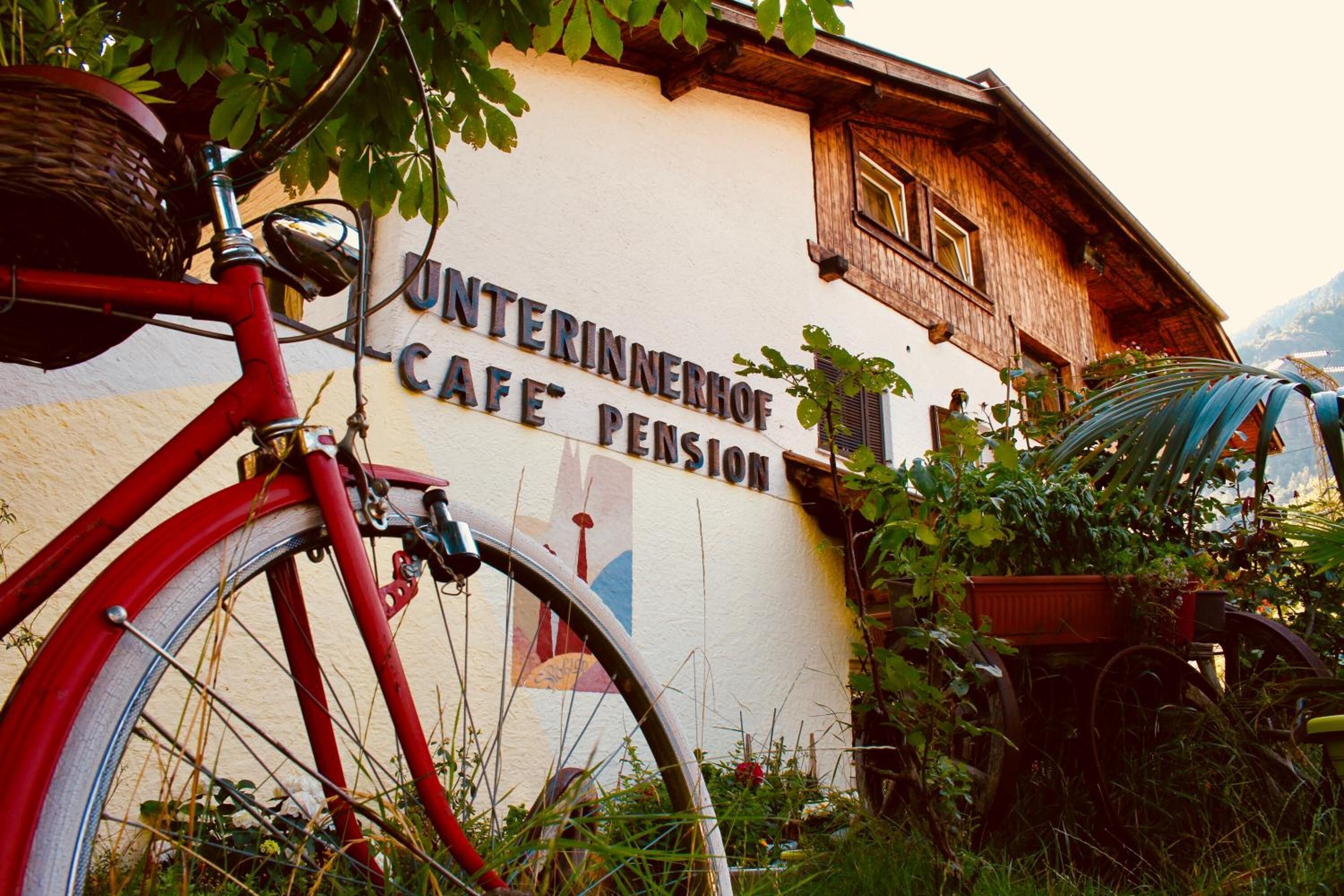 A red bicycle parked in front of a building with a sign that reads "Unterinnerhof Cafe Pension".