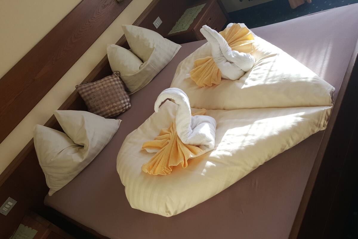 A neatly made bed with towels arranged in swan shapes, pillows, and a checkered throw blanket.