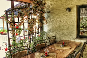 A rustic dining area with a wooden table, wicker chairs, and a view of a garden through a window with climbing roses. - Hotel Unterinnerhof (Renon)