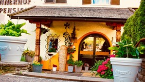 A traditional building with a yellow facade, wooden beams, and a tiled roof. There are potted plants and a sign that reads "INNERHOF PENSION." - Hotel Unterinnerhof (Renon)