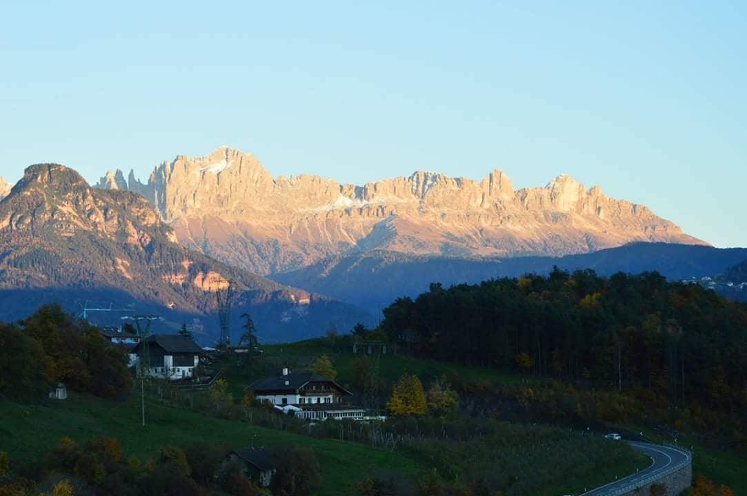 A mountainous landscape with a winding road and a few houses in the foreground.