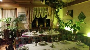 A dining area with tables set for a meal, surrounded by potted plants and draped curtains. - Hotel Unterinnerhof (Renon)