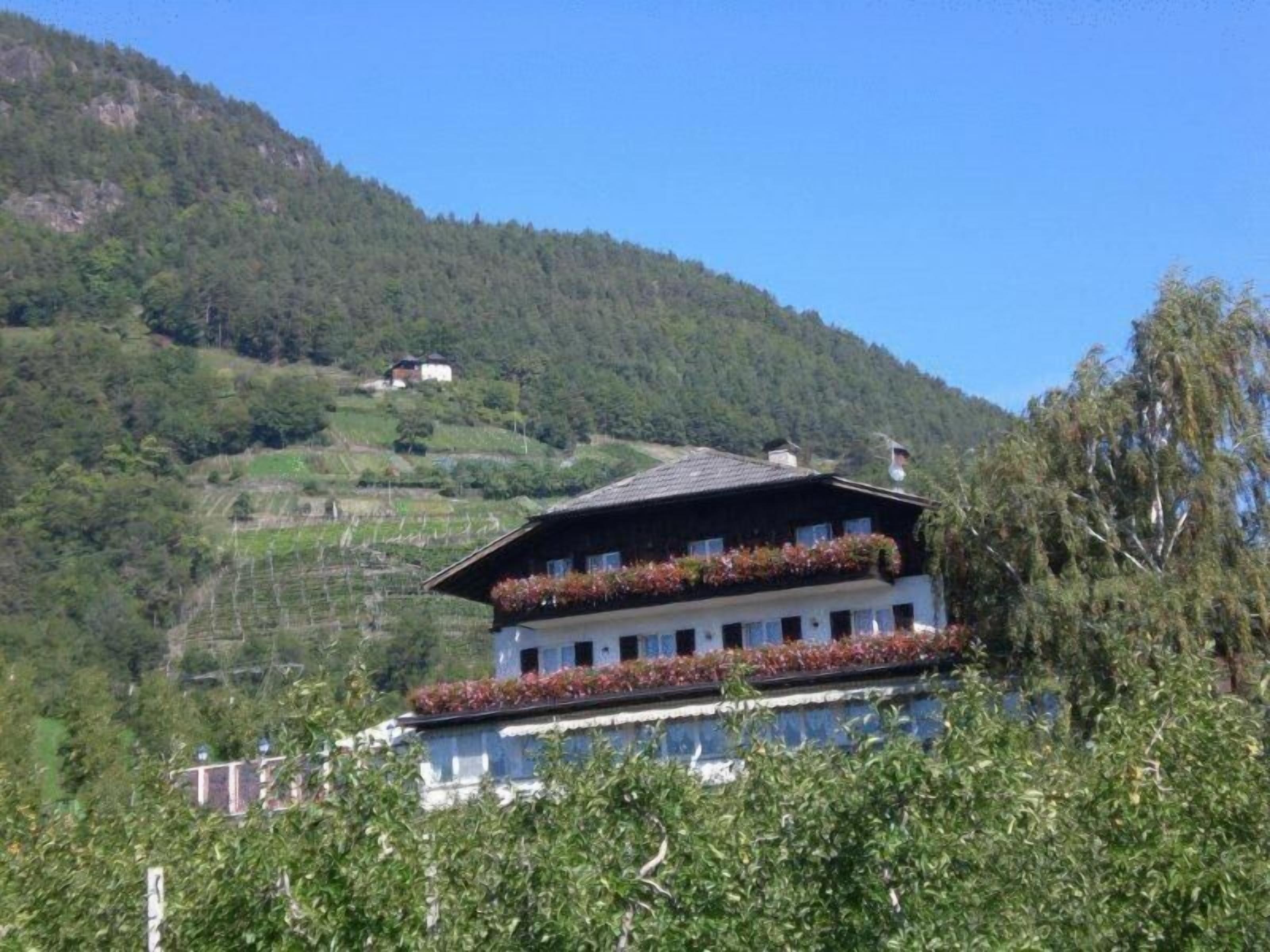 A two-story building with a sloped roof, surrounded by lush greenery and hills.