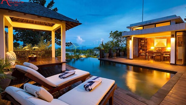 Ein luxuriöser Poolbereich im Freien mit Liegestühlen, einer überdachten Lounge und einem modernen Gebäude mit warmer Beleuchtung.