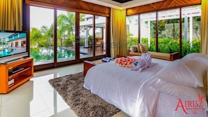 Ein Schlafzimmer mit einem großen Bett, einem Fernseher und Blick auf einen Pool und Grünflächen.