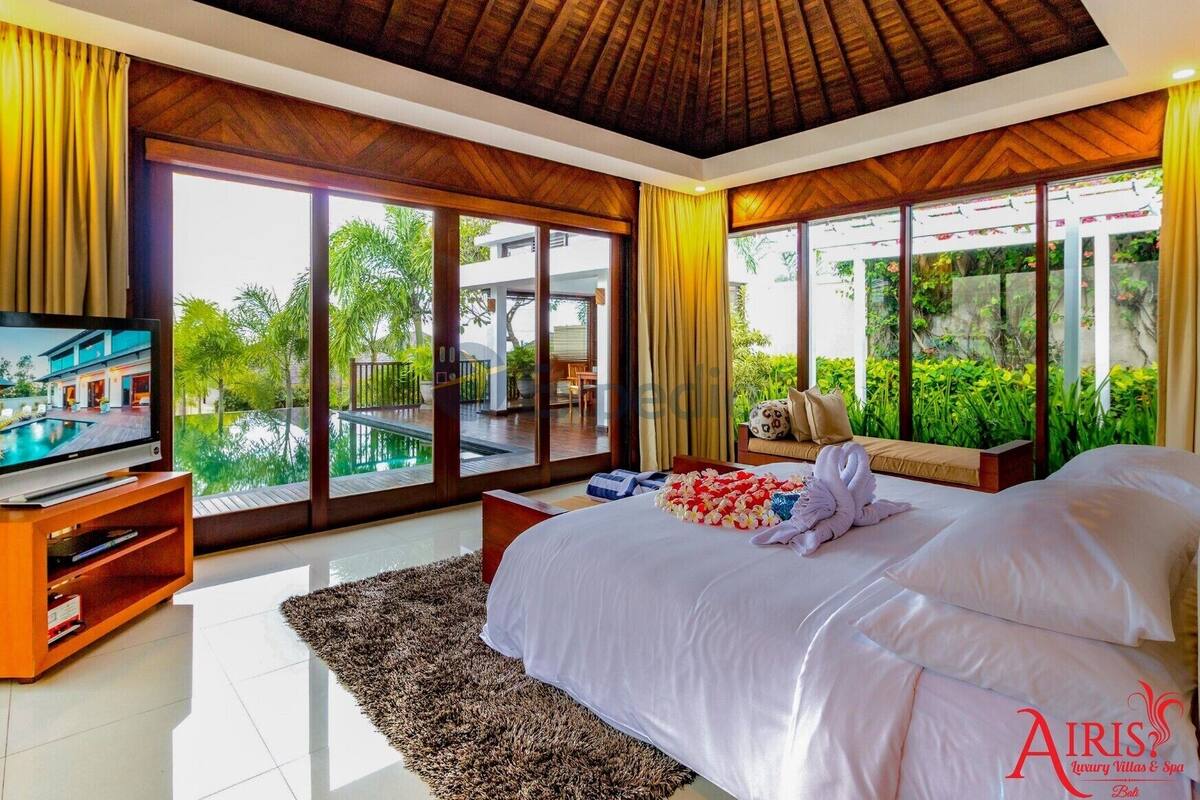 Un dormitorio con una cama grande, televisión y vistas a una piscina y follaje.
