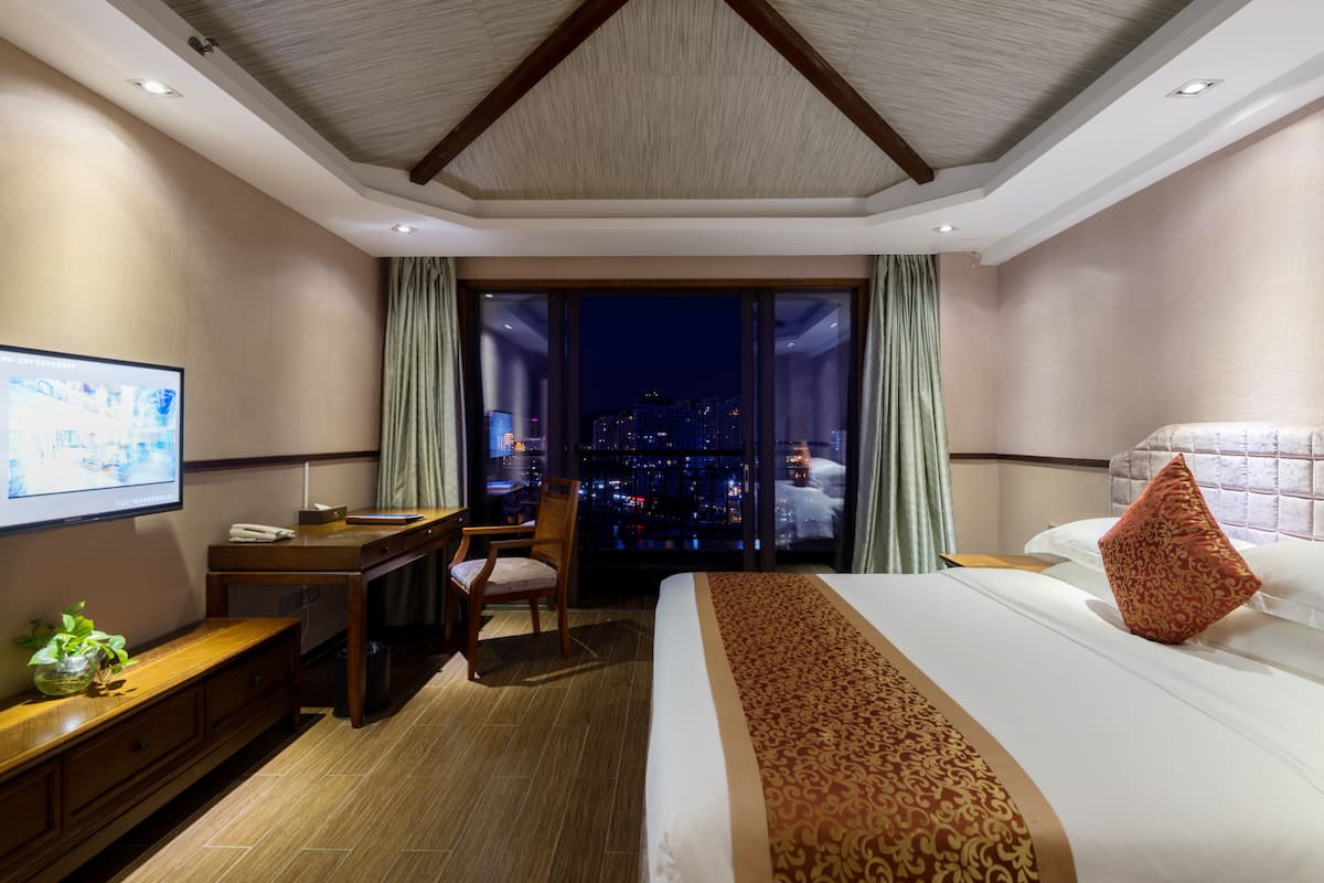 Une chambre d’hôtel avec un grand lit, un bureau, une chaise et un téléviseur fixé au mur.