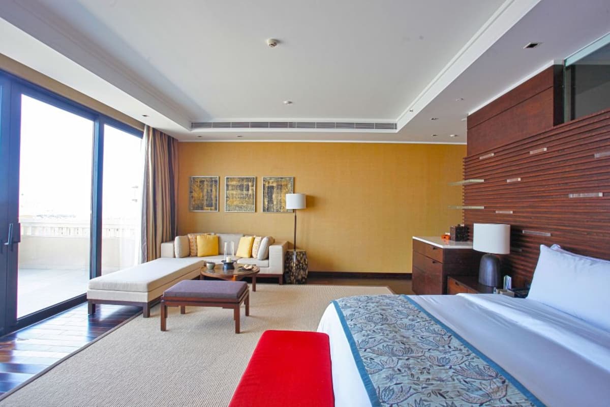 A hotel room with a large bed, a sofa, a desk, and a view of the outdoors.