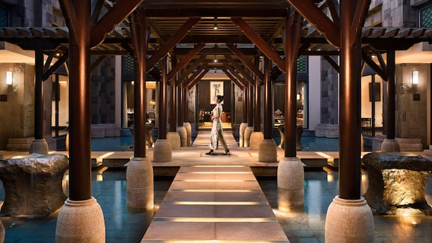 A corridor with stone pillars and a person walking. - Raffles Hainan (Lingshui)