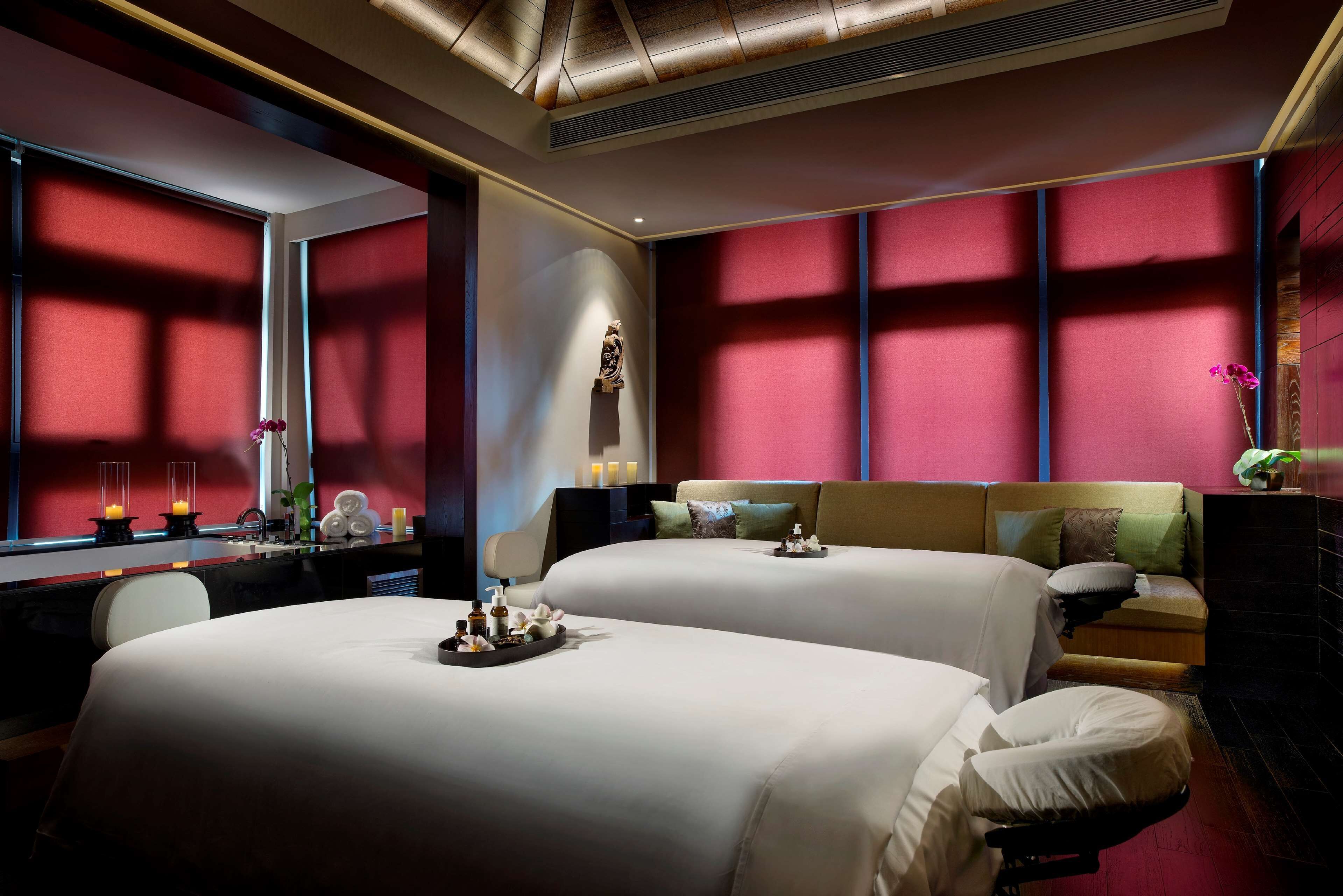 A hotel room with two beds, a desk, and a large window with red curtains.