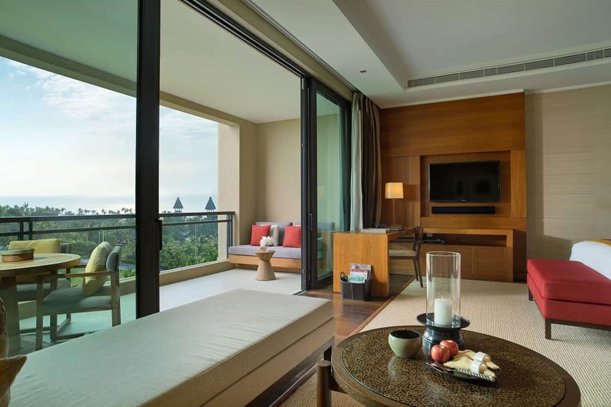 A hotel room with a balcony, a sofa, a TV, and a dining area with a table and chairs.
