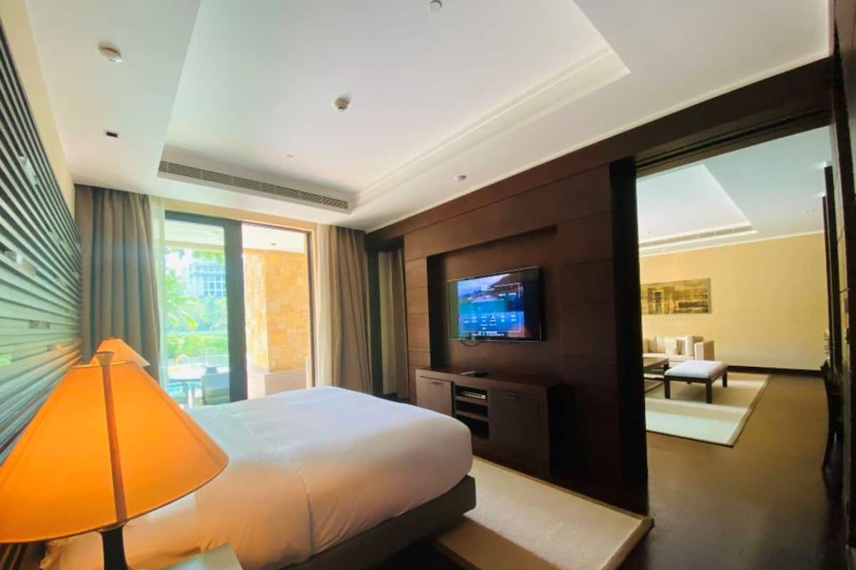 A modern hotel room with a large bed, a TV mounted on the wall, and a view of the outside through a sliding door.