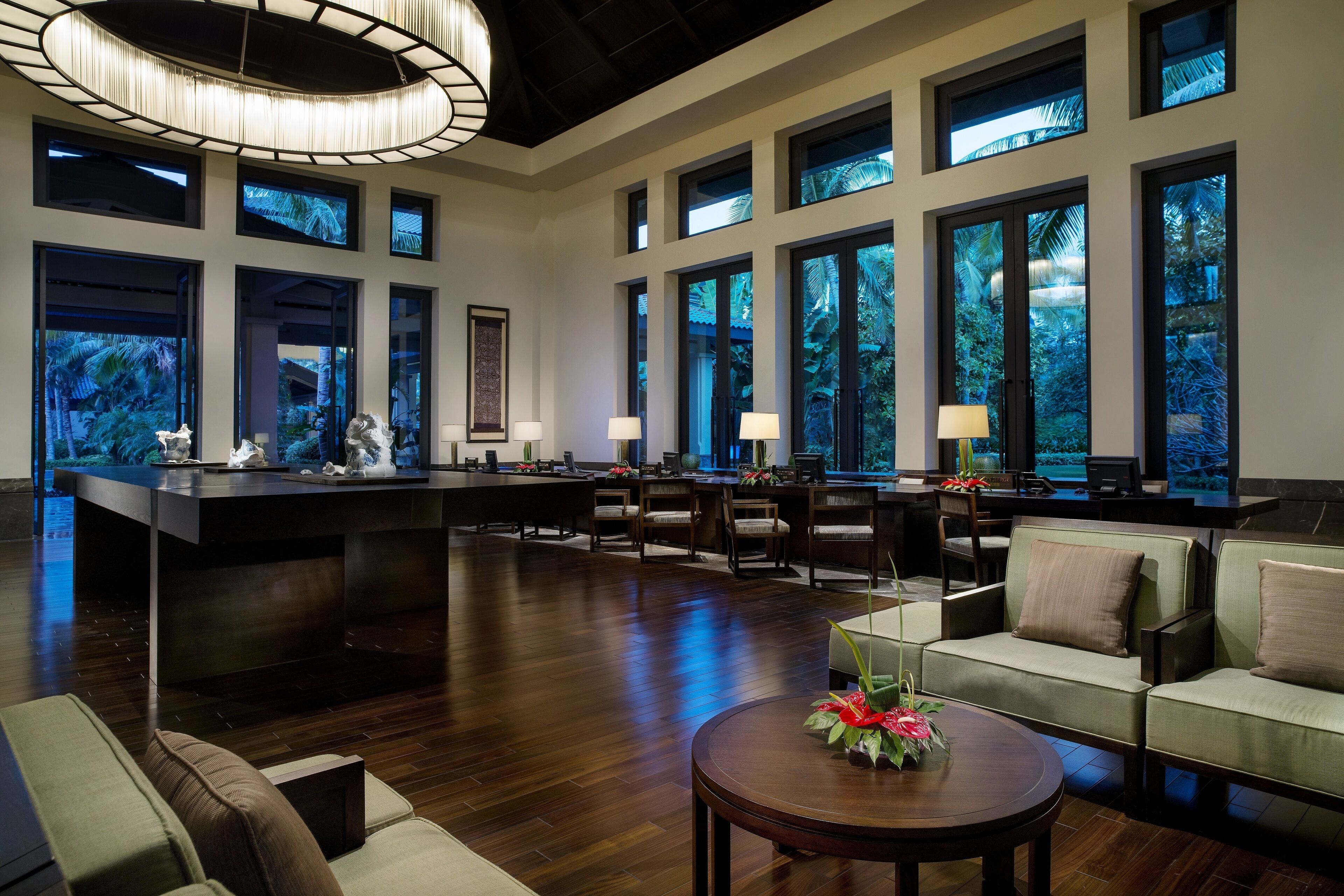 A spacious lobby with a central bar, multiple seating areas, and large windows offering views of greenery.