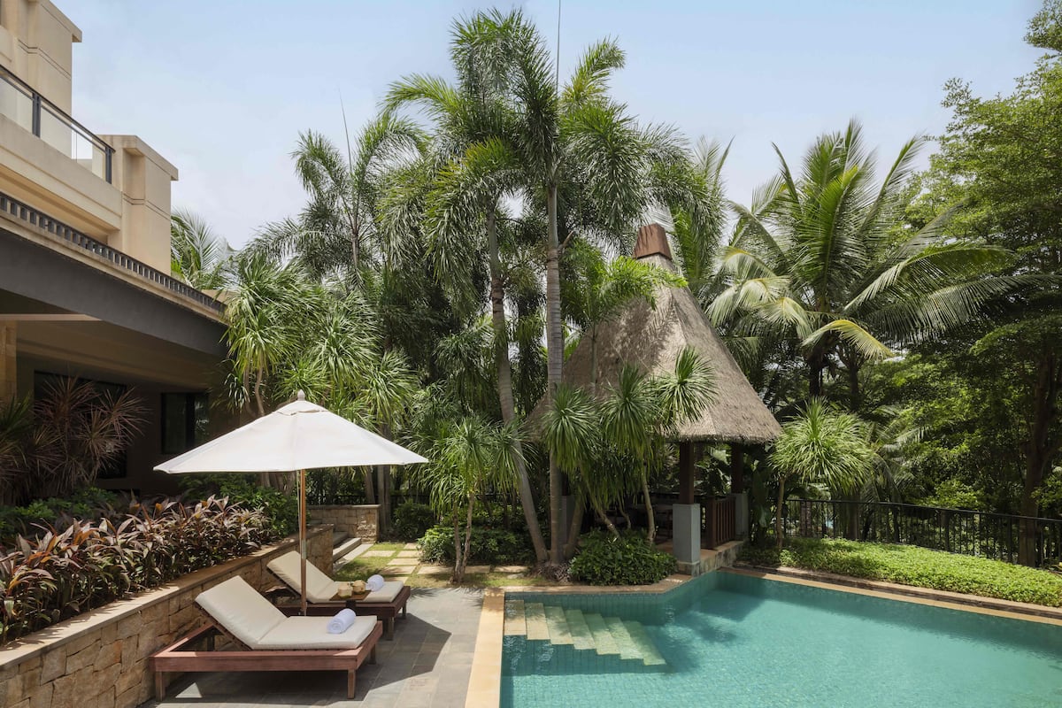 A pool area with lounge chairs and a thatched-roof structure.