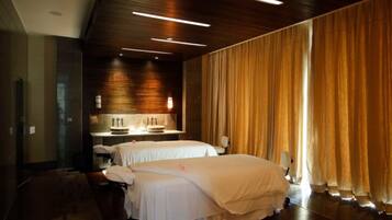 Two beds with crisp linens, a stylish table, and a large window with curtains.
