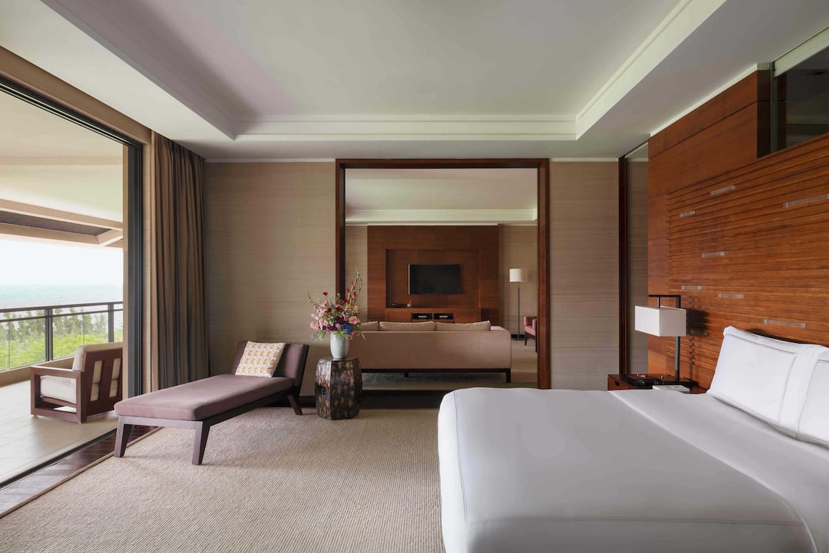A hotel room with a large bed, a sofa, a small table with a vase of flowers, and a view of the outdoors.