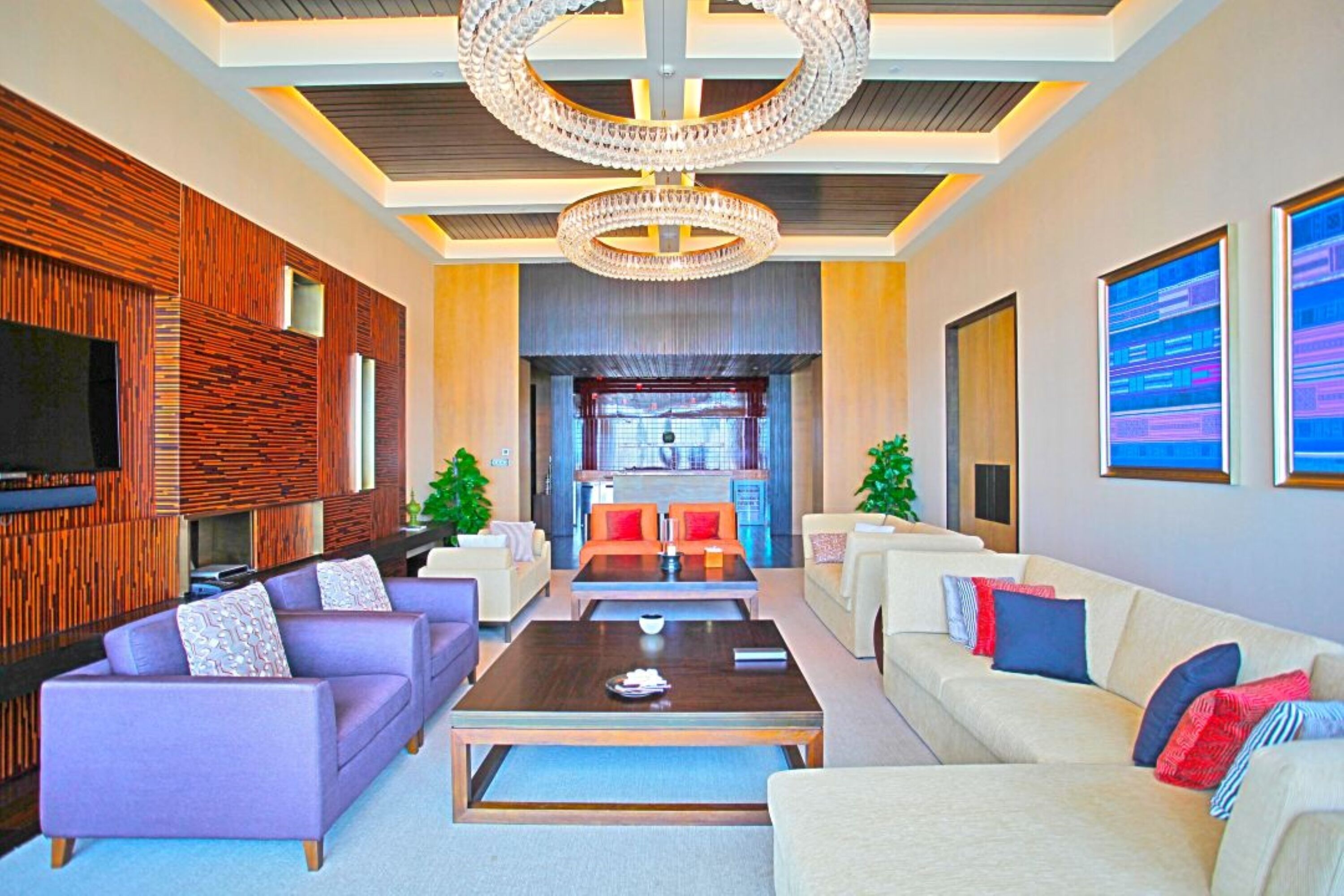 A modern living room with a large TV, sofas, a coffee table, and a chandelier.