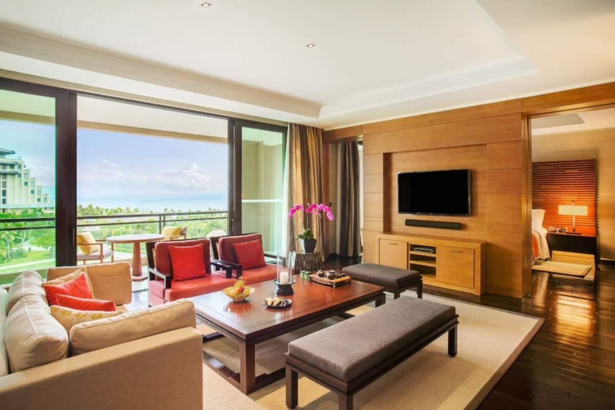 A modern hotel room with a large balcony, a flat-screen TV, and a cozy seating area with a coffee table.
