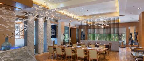 A spacious restaurant with wooden flooring, stone pillars, and a modern ceiling design.