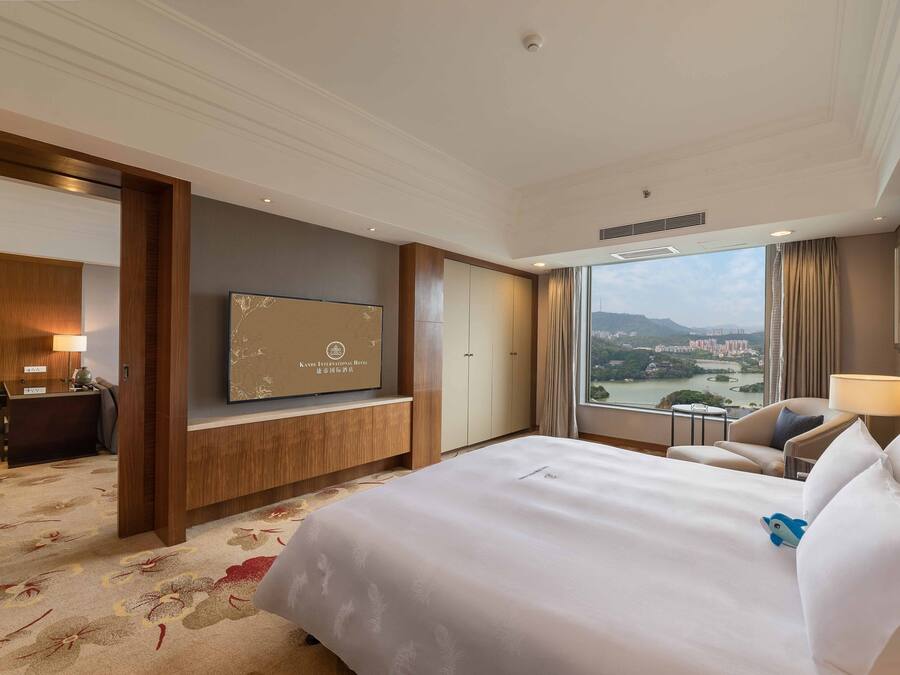 A hotel room with a large bed, a desk, a television, and a view of a cityscape.
