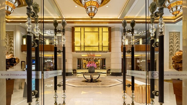 Un amplio vestíbulo con candelabros, un arreglo floral central y letreros de Kande International Hotel.