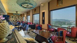 Un salón amplio con muebles modernos, ventanas grandes con vistas a la ciudad y detalles decorativos en el techo.