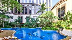 Una piscina rodeada de abundante vegetación y palmeras, con un edificio al fondo.