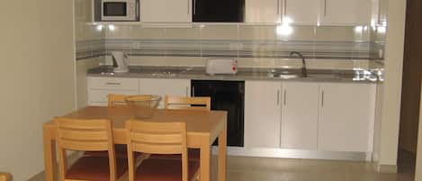Cocina compacta con armarios blancos, microondas, tostadora y pileta. Hay una mesa de comedor de madera con sillas.