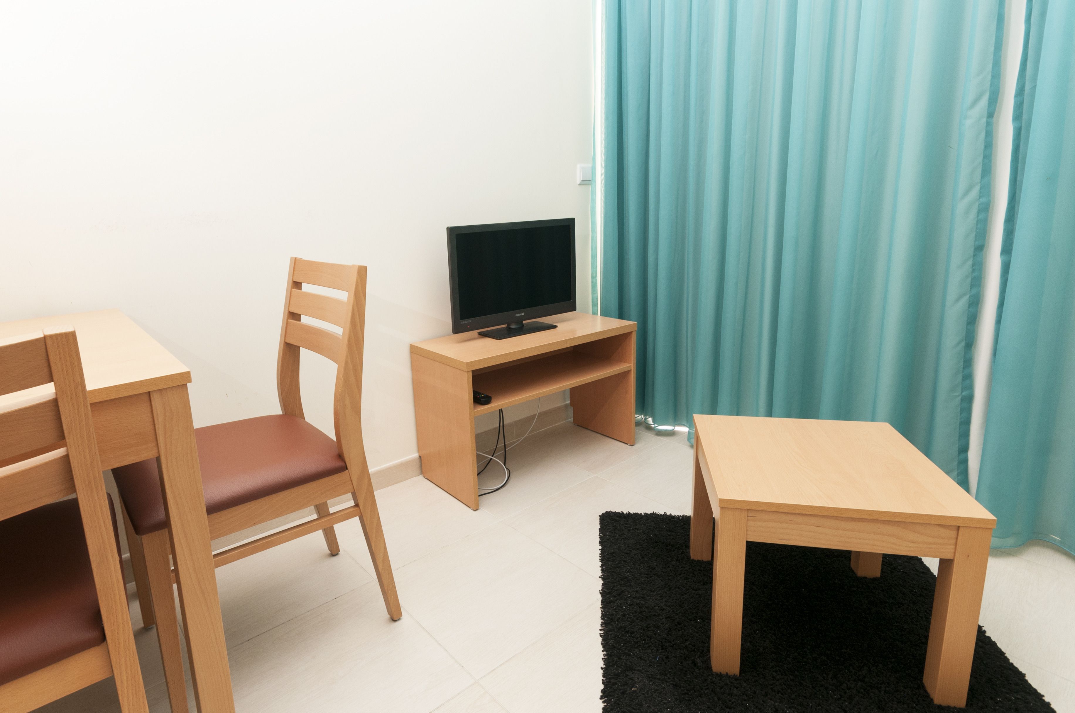 A small room with a wooden desk, a chair, a television on a stand, and a black rug.