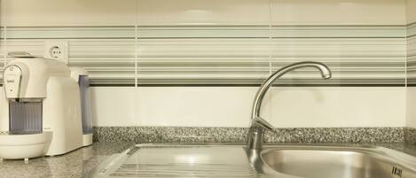 A kitchen with a stainless steel sink, a coffee maker, and a tiled backsplash.