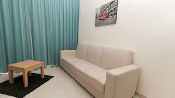 Un salon avec un canapé beige, une petite table en bois, un tapis noir et un rideau bleu.