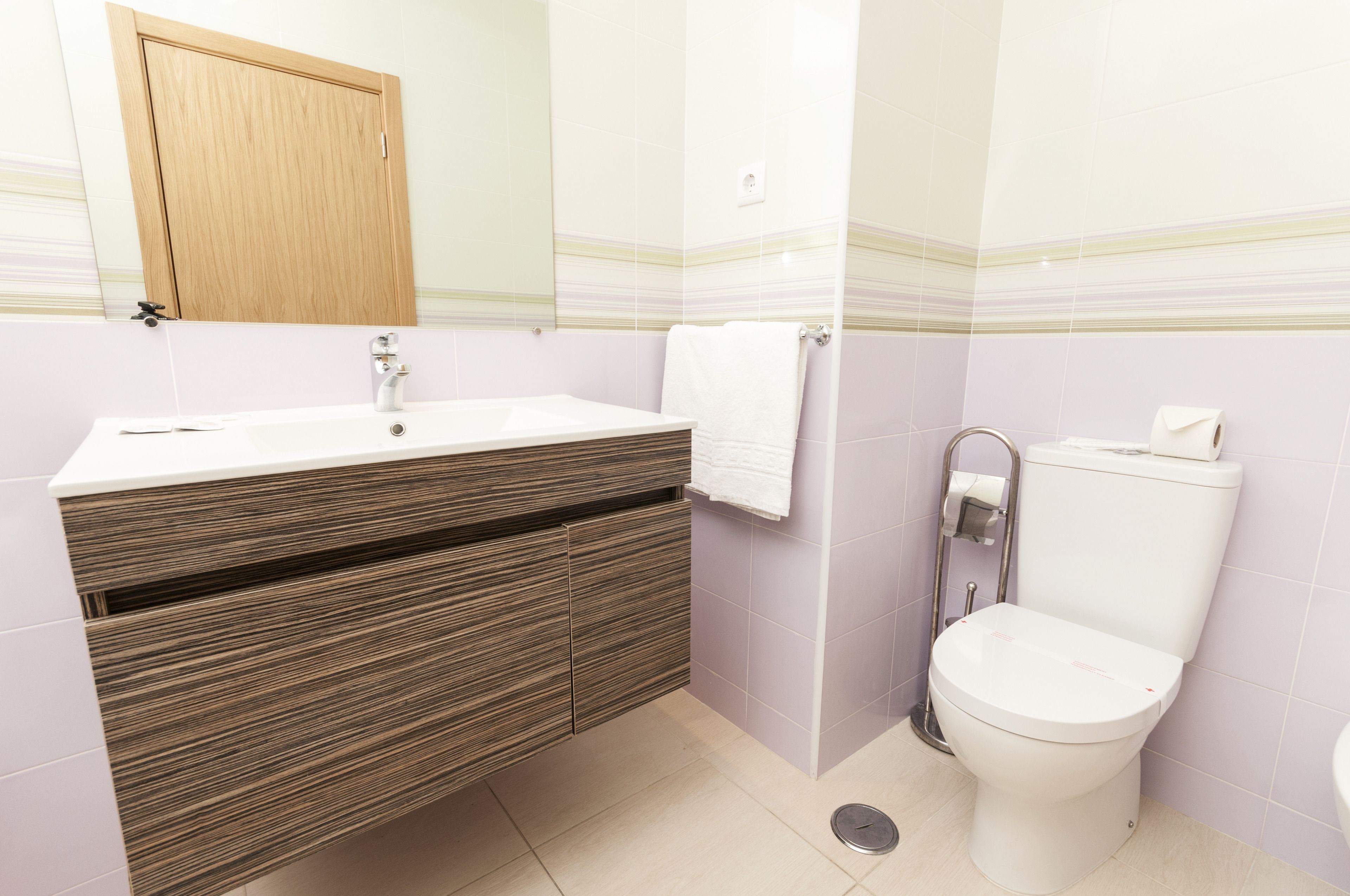 A bathroom with a wooden vanity, a white sink, a toilet, and a mirror above the vanity.