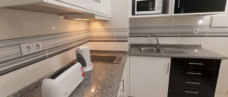 A modern kitchen with white cabinets, a built-in microwave, a toaster, and a sink.